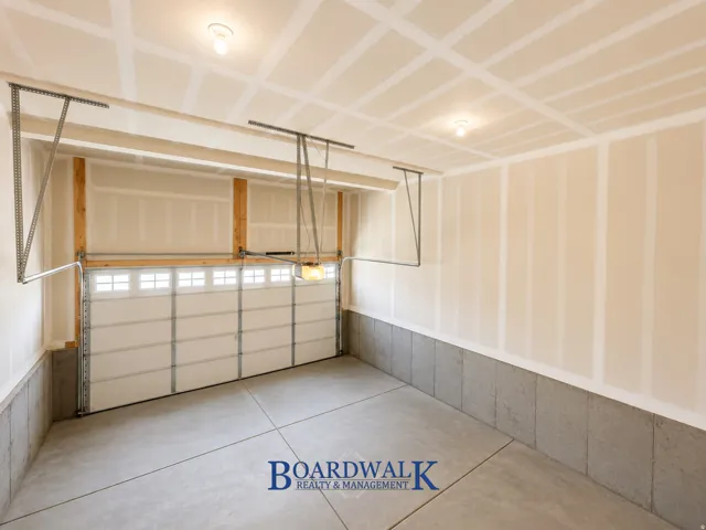 Spacious garage featuring a sectional overhead door with upper window panels, exposed wood framing, concrete flooring, and built-in overhead lighting