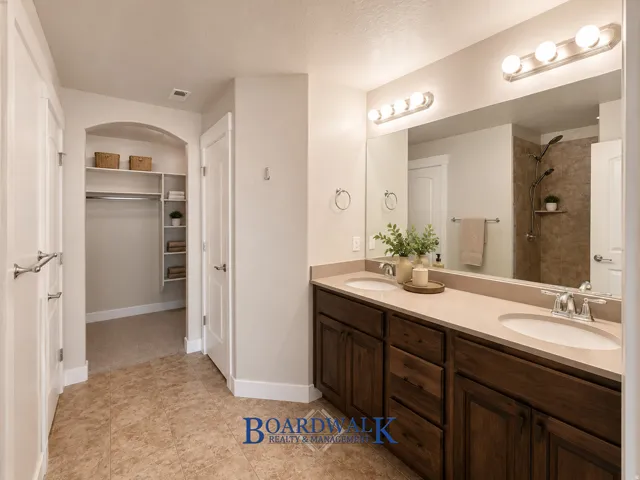 Dual basin vanity with undermount sinks, warm wood cabinetry, and a large wall-mounted mirror with overhead lighting