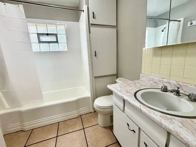 Bathroom featuring a white bathtub, glass block window, floor-mounted toilet, and a vanity with a white countertop