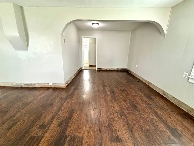 Interior room featuring wood-finish flooring, light-toned wall paint, and a decorative archway