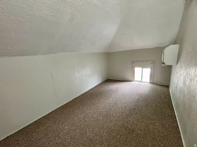 Carpeted room with a pitched ceiling and a window featuring a blind