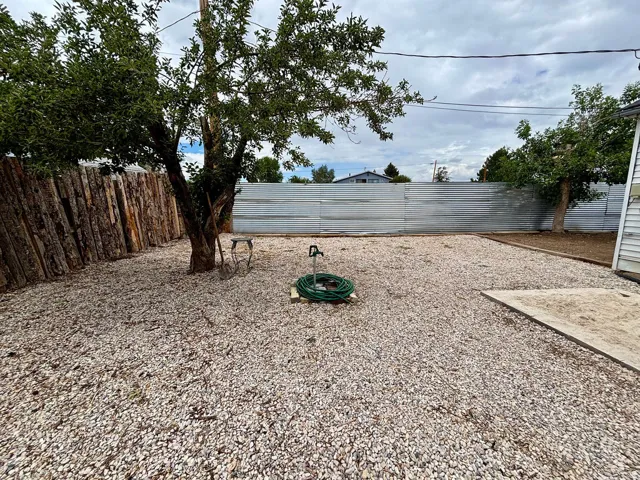 Expansive backyard featuring a gravel surface, mature trees, a wood-plank fence, and a corrugated metal fence
