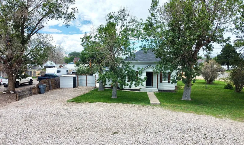 White exterior with dark roof shingles, framed by mature trees