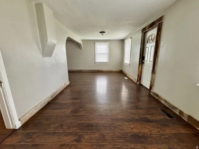 Expansive room featuring wood-finish flooring, light-toned walls, and a decorative arched entryway