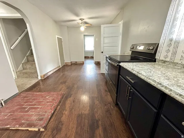 Open concept living space featuring wood-finish flooring, a ceiling fan, and a kitchen area with black cabinetry, stainless steel appliances, and light-colored countertops