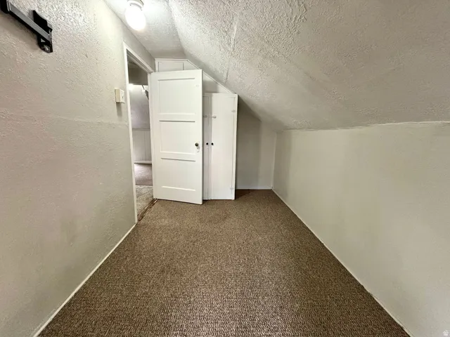 Carpeted attic space with sloped ceilings and a flush-mount light fixture