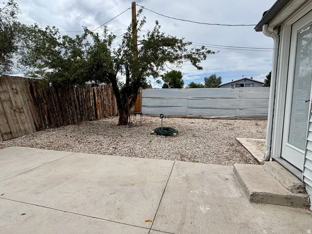 Expansive gravel yard featuring a concrete patio, mature tree, wood plank fencing, and corrugated metal fencing