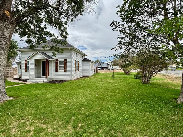White siding residence featuring a covered front entry with wood columns, dark shutters, and a front lawn with mature trees