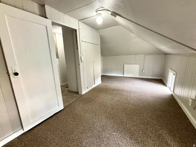 Carpeted room with a pitched ceiling and white paneled walls