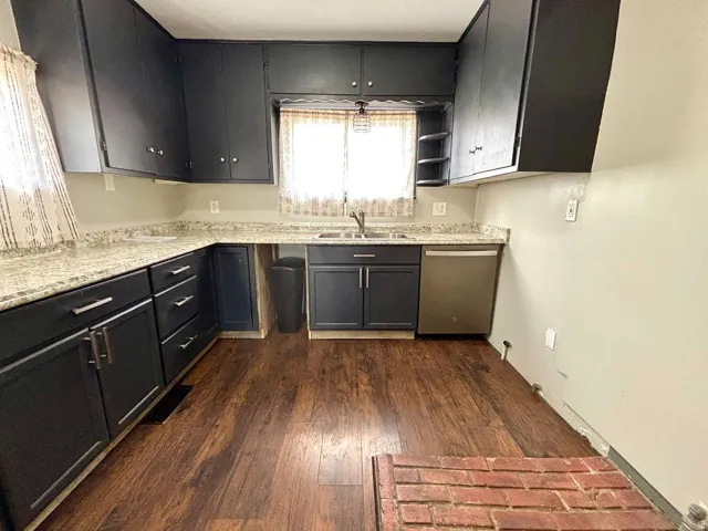 Kitchen featuring dark cabinetry with silver-tone hardware, a stainless steel dishwasher, a double basin sink, and light-toned countertops