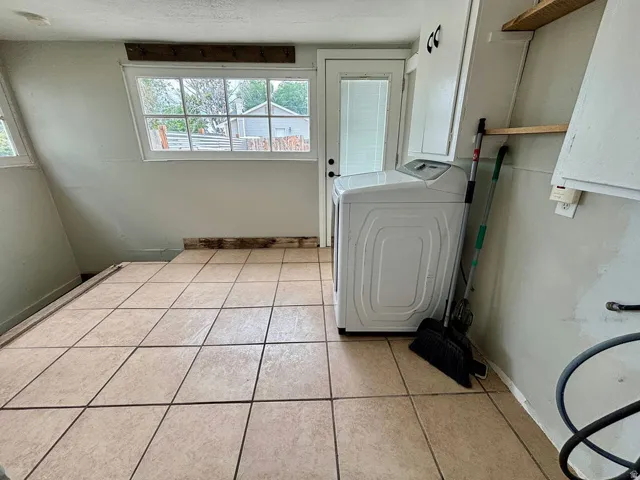 Tiled flooring throughout this utility space, featuring white upper cabinetry and a rear access door with integrated blinds