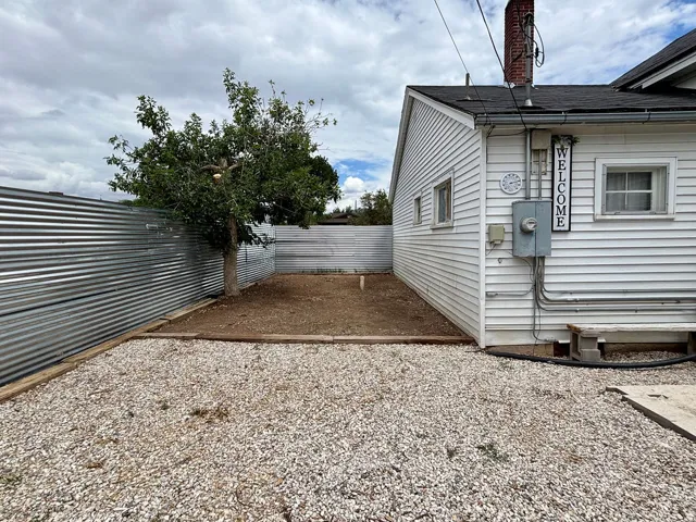 Gravel outdoor area with a corrugated metal fence and mature tree