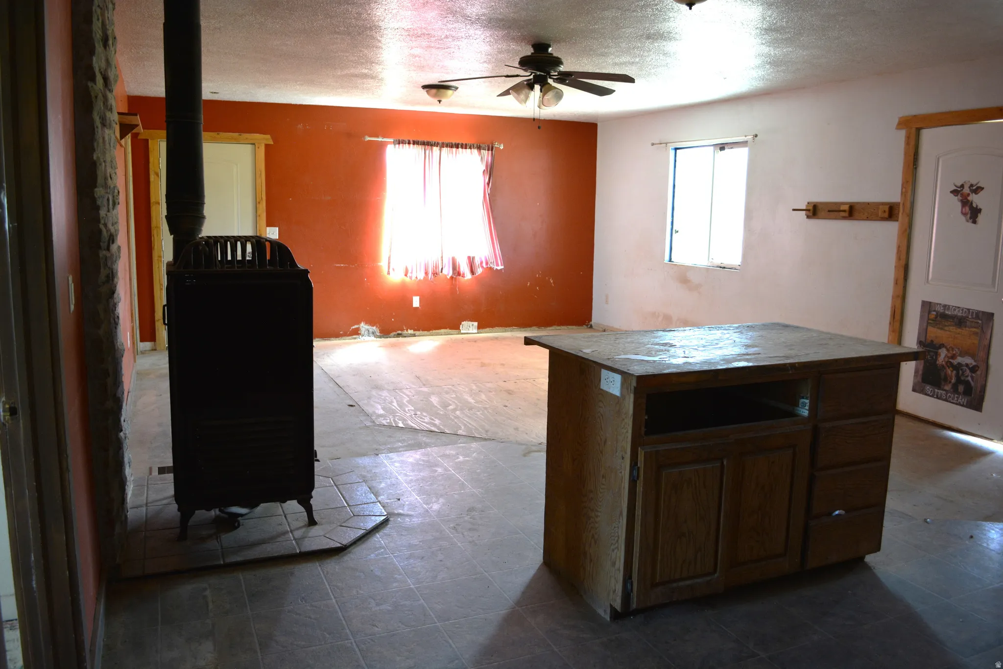 Open concept room featuring a built-in wood-burning stove with a stone surround, a ceiling fan, and tile flooring
