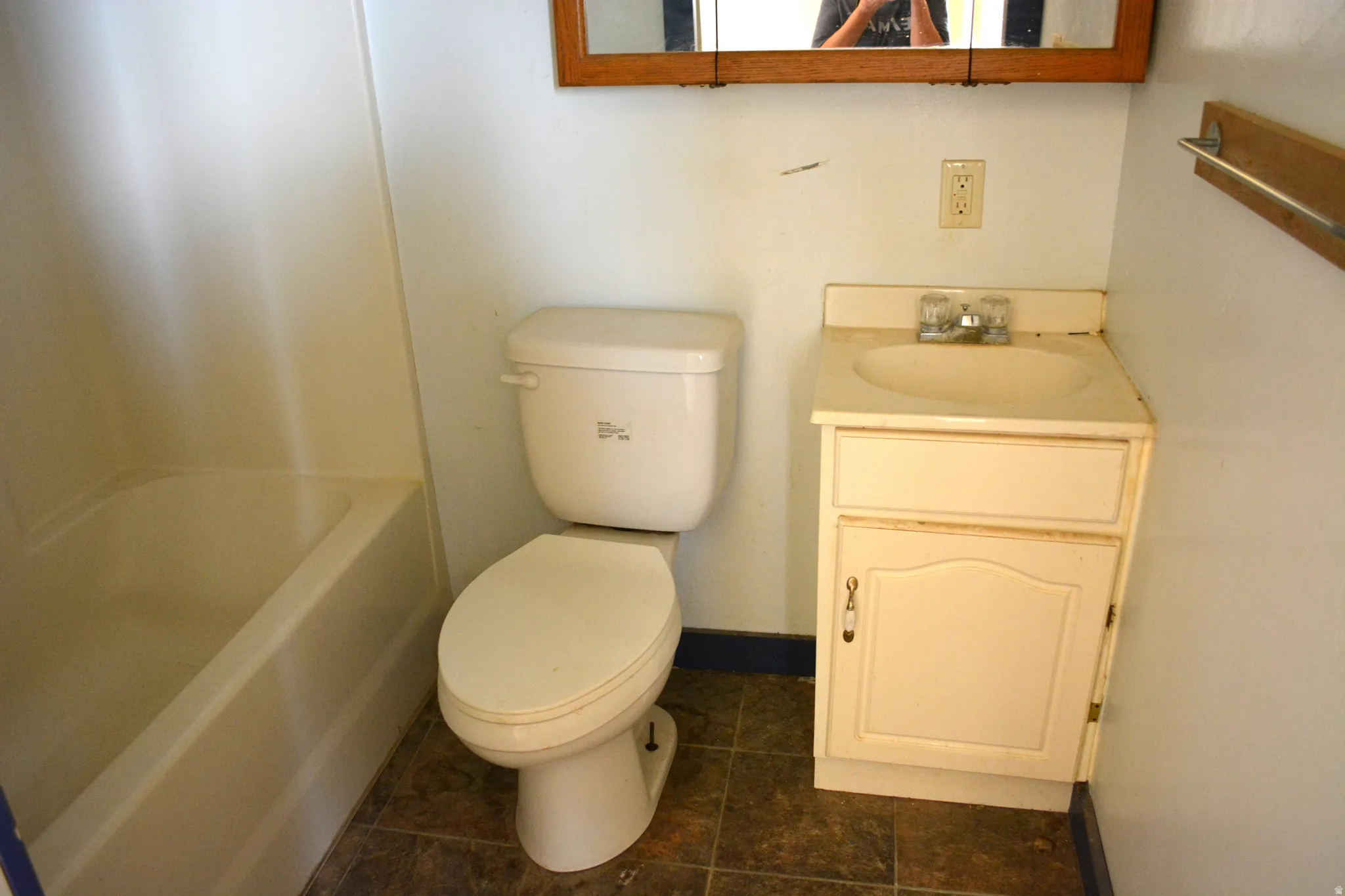 Bathroom featuring a built-in tub, white toilet, single vanity with integrated sink, and an overhead medicine cabinet with a wood-finish frame