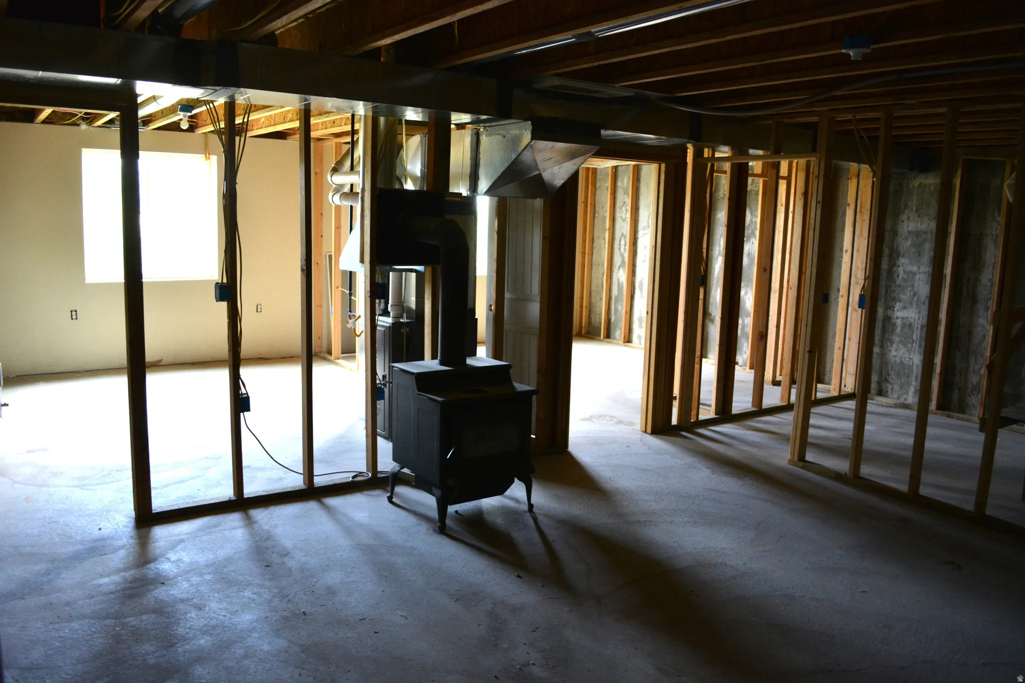 Unfinished basement featuring exposed wood framing, concrete flooring, and a freestanding wood-burning stove