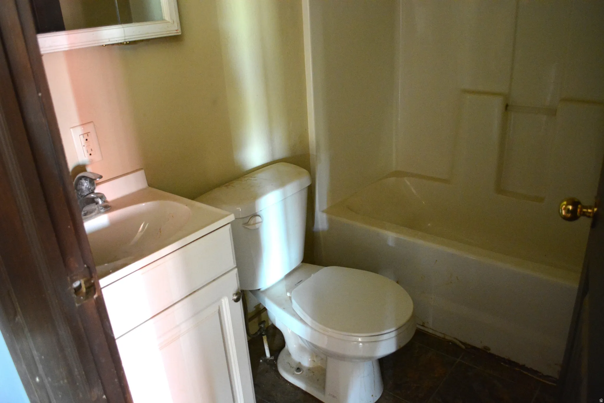 Bathroom featuring a white vanity with integrated sink, chrome faucet, white toilet, and a white bathtub with a shower surround