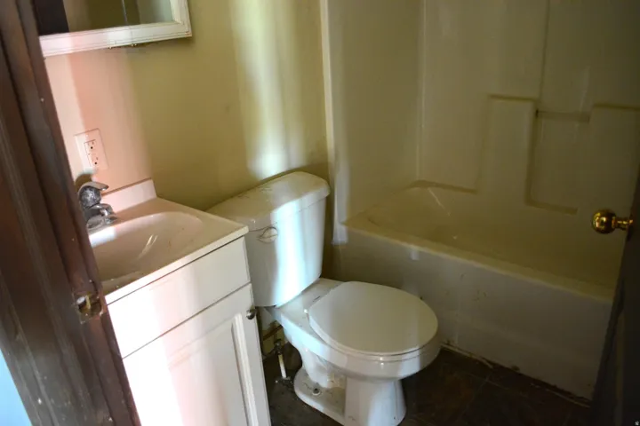 Bathroom featuring a white vanity with integrated sink, chrome faucet, white toilet, and a white bathtub with a shower surround