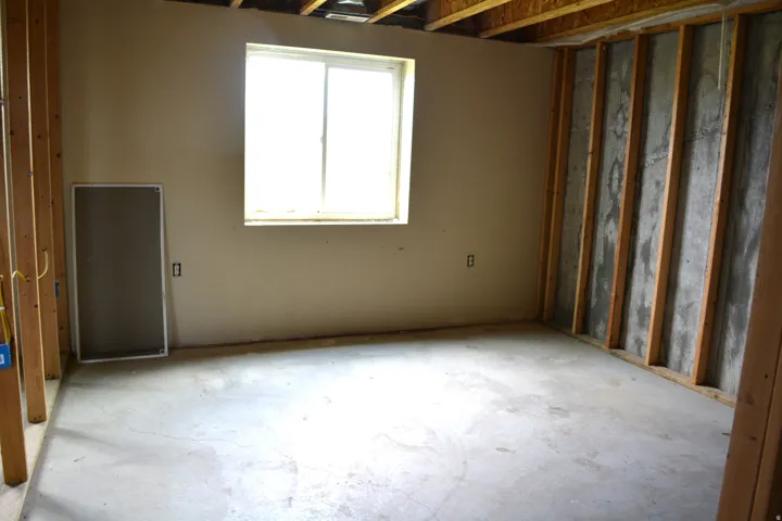 Unfinished basement room featuring a window, concrete flooring, wooden wall studs, and exposed ceiling joists