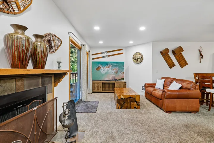 Living area featuring a stone-faced fireplace with a wood mantle, carpet flooring, recessed lighting, and a glass sliding door