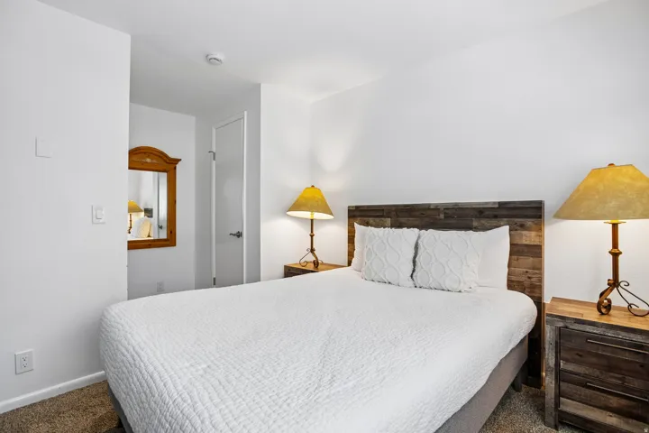 Bedroom featuring a wood-finish headboard, wood-finish nightstands, wall-to-wall carpeting, and bright white walls