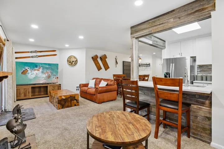 Open-concept living space featuring recessed lighting, a kitchen pass-through with a breakfast bar, white cabinetry, a stainless steel refrigerator, and wood-finish accents