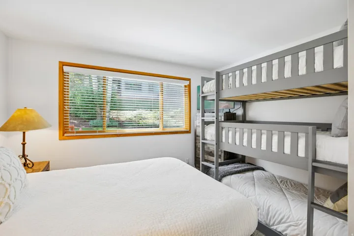 Bright sleeping area featuring a triple bunk bed, a window with wood framing, and white walls