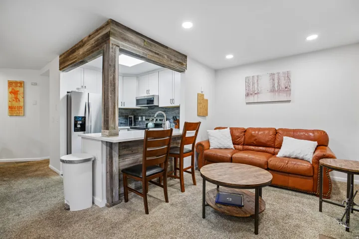 Open-concept living space featuring a breakfast bar with seating, wood-finish accents, white cabinetry, stainless steel appliances, and recessed lighting