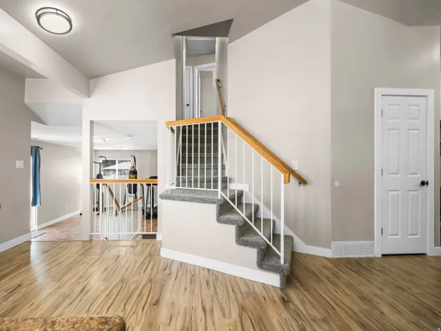 Light wood-finish flooring extending into various areas, complemented by a carpeted staircase with white balusters and a wood handrail