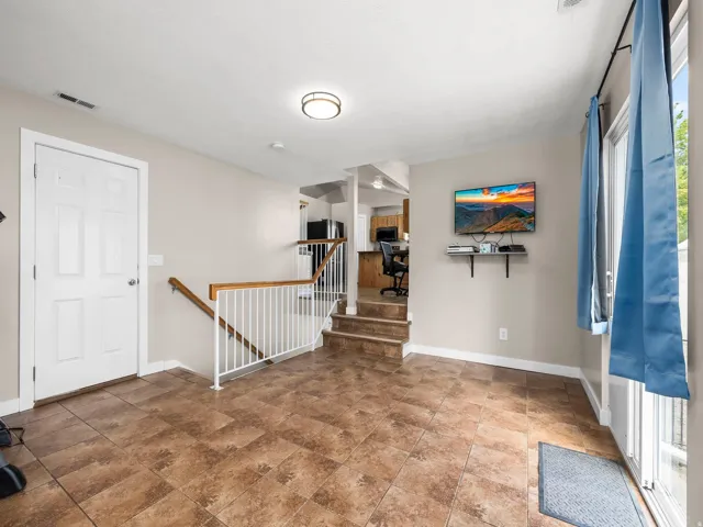 Spacious room featuring tile flooring, a white paneled door, and access to a multi-level staircase with wood handrails and white balusters