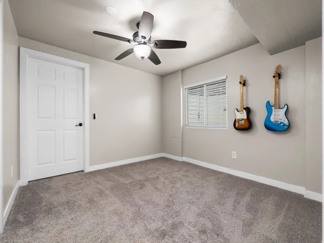 Spacious room featuring neutral carpeting, a white paneled door, and a ceiling fan with integrated lighting