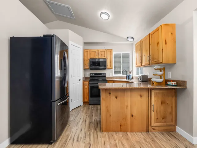 Kitchen featuring wood-finish flooring, natural wood cabinetry, a built-in kitchen island, granite-style countertops, and a full suite of black appliances