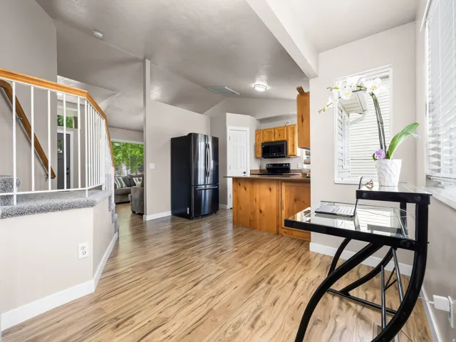 Open-concept living space featuring wood-finish flooring, a contemporary staircase with white balusters, and a kitchen with solid wood cabinetry and black appliances