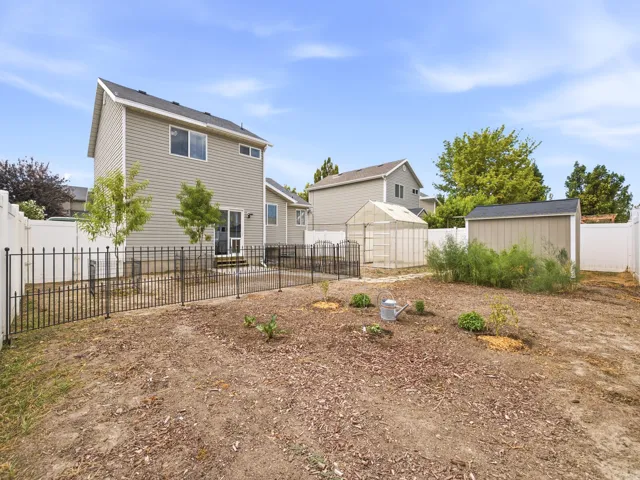 Spacious backyard featuring a storage shed, a greenhouse structure, and a perimeter of white privacy fencing