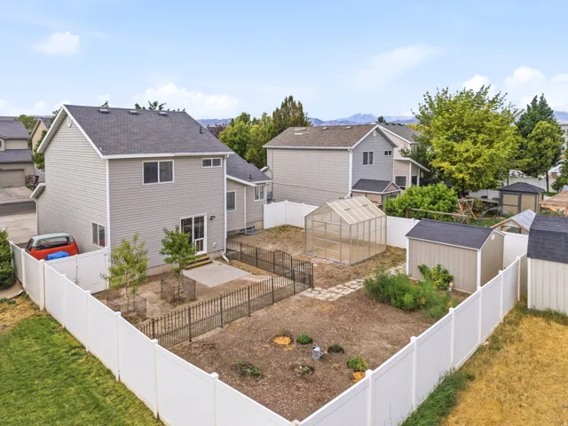 Fenced backyard featuring a greenhouse, two storage sheds, and a concrete patio