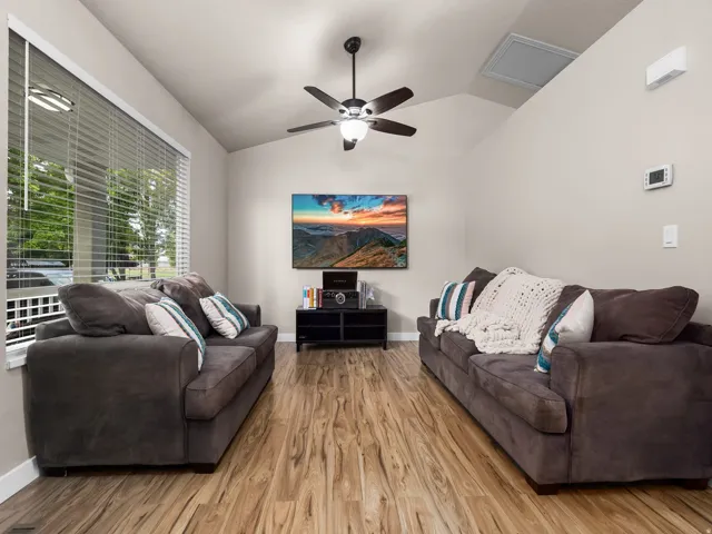 Living area featuring wood-finish flooring, a vaulted ceiling, and a ceiling fan with integrated lighting