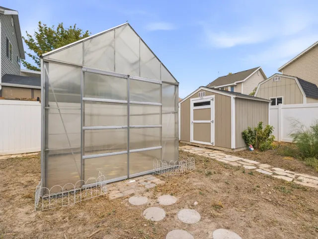 Backyard featuring a greenhouse, a storage shed with a shingle roof, a stepping stone pathway, and vinyl fencing