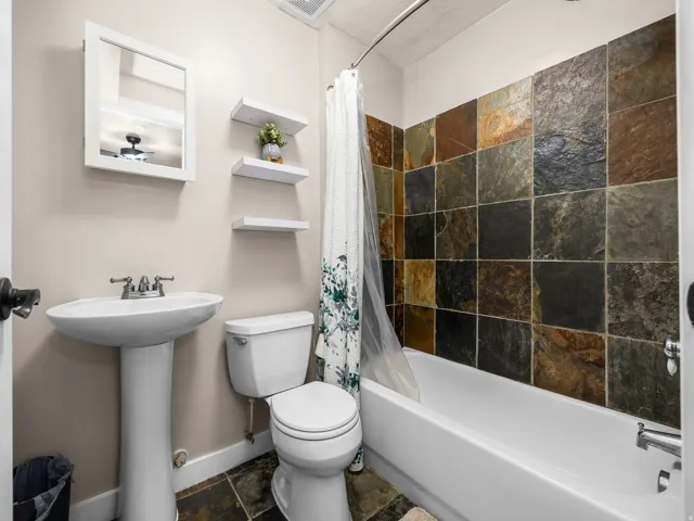 Bathroom featuring a pedestal sink, white toilet, and a bathtub with a natural stone tile surround
