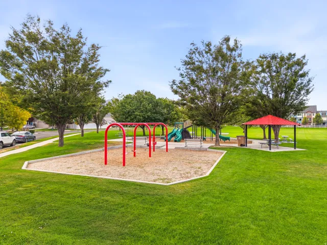 Community playground featuring swing sets, multiple slides, a covered picnic area with tables, and mature trees providing shade