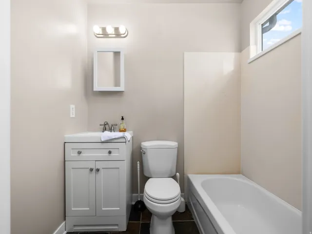 Bathroom featuring a white vanity with cabinet storage, a wall-mounted medicine cabinet, a three-bulb light fixture, a toilet, and a white bathtub