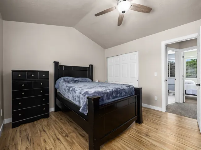Vaulted ceiling bedroom featuring wood-finish flooring, a ceiling fan with integrated lighting, and bi-fold closet doors