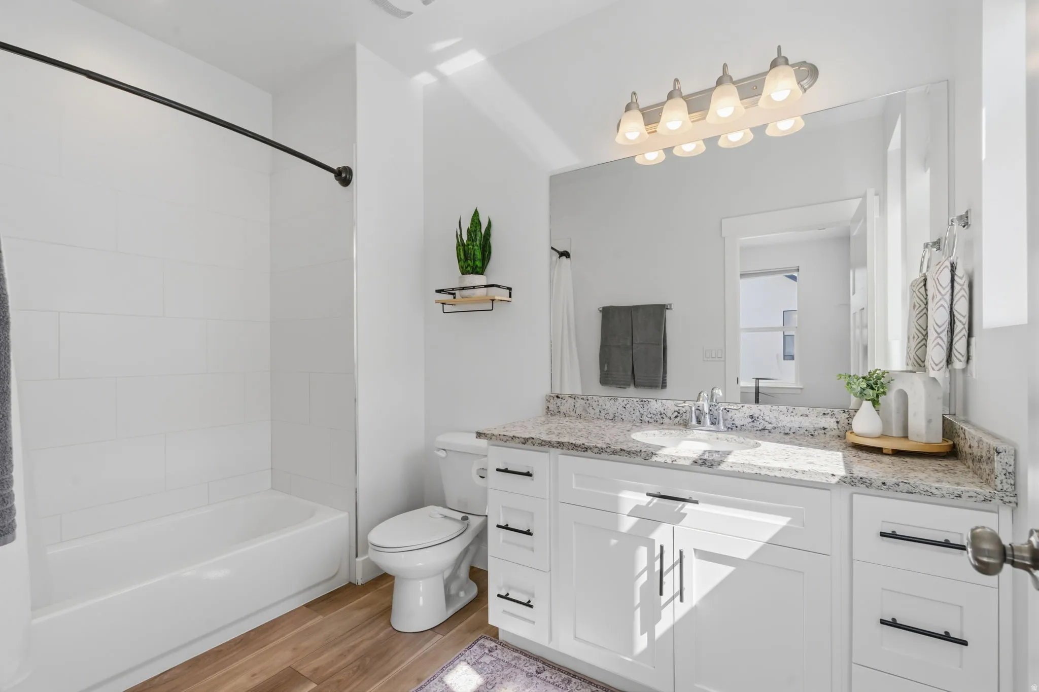 Bathroom featuring a white subway tile tub surround, wood-finish flooring, a white vanity with a light-colored countertop, and a large wall-mounted mirror
