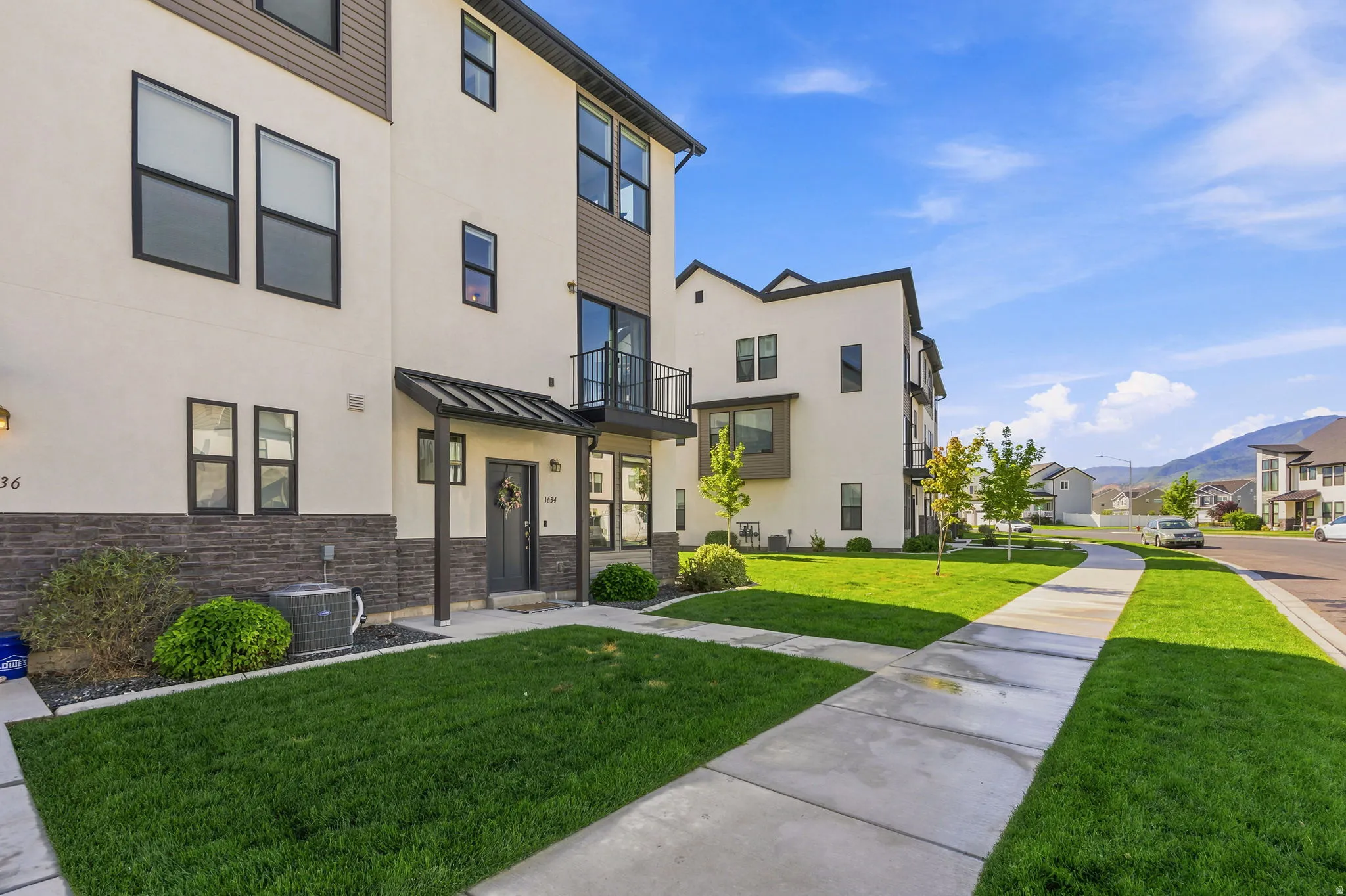 Contemporary townhome exterior featuring a stucco finish, stone veneer accent, and a covered entry
