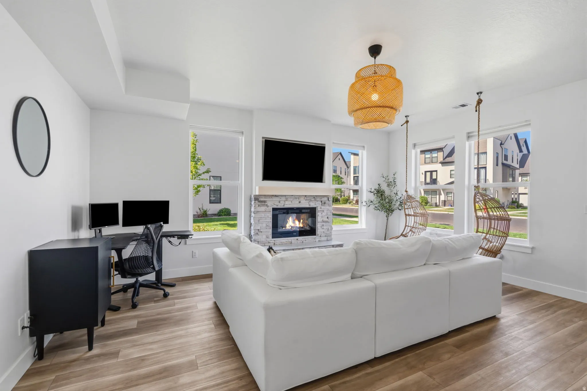 Living area featuring wood-finish flooring, a stone-clad fireplace, and multiple windows providing natural light