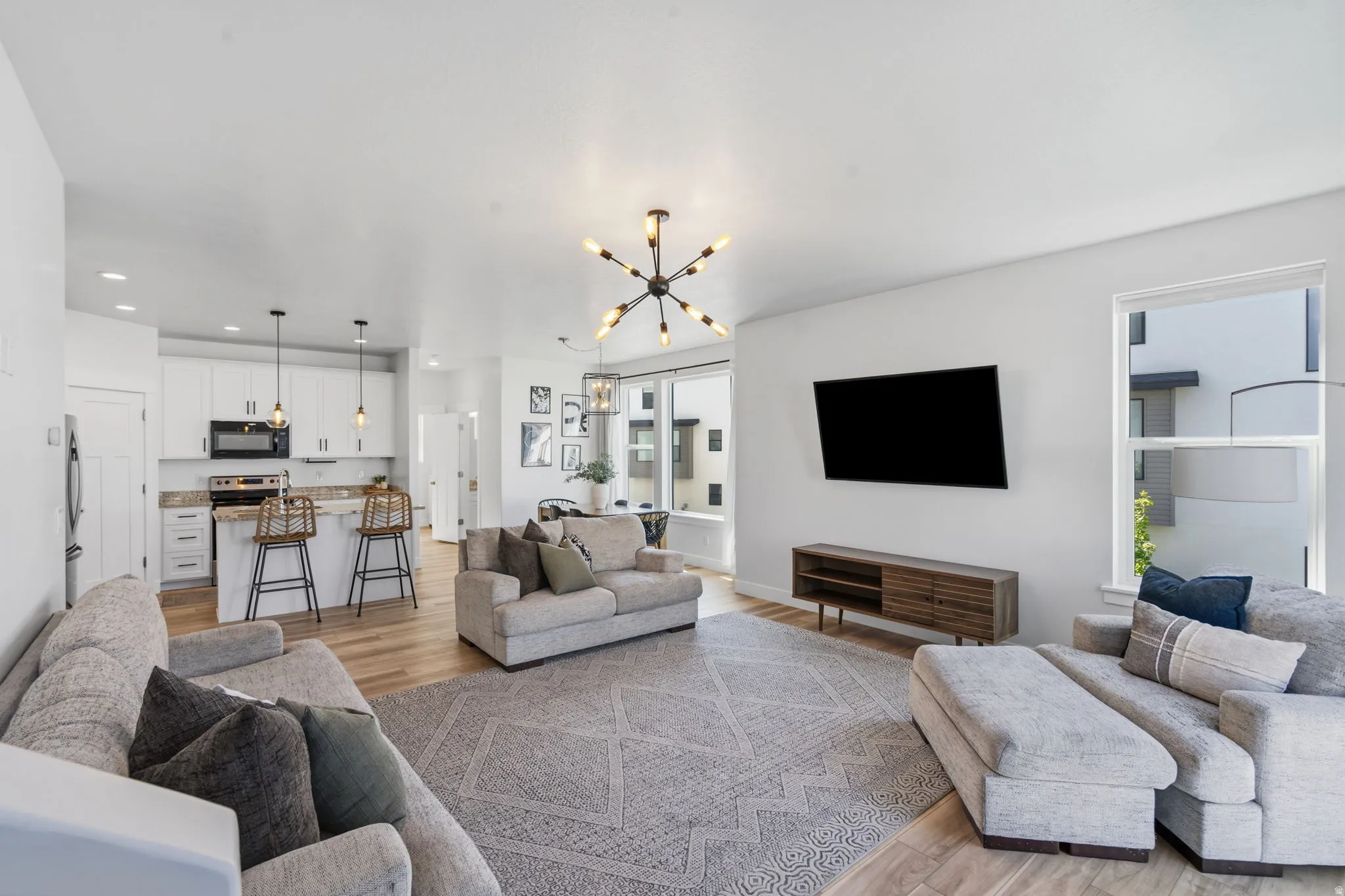 Spacious open-concept living area featuring wood-finish flooring, a modern sputnik chandelier, and expansive windows providing ample natural light