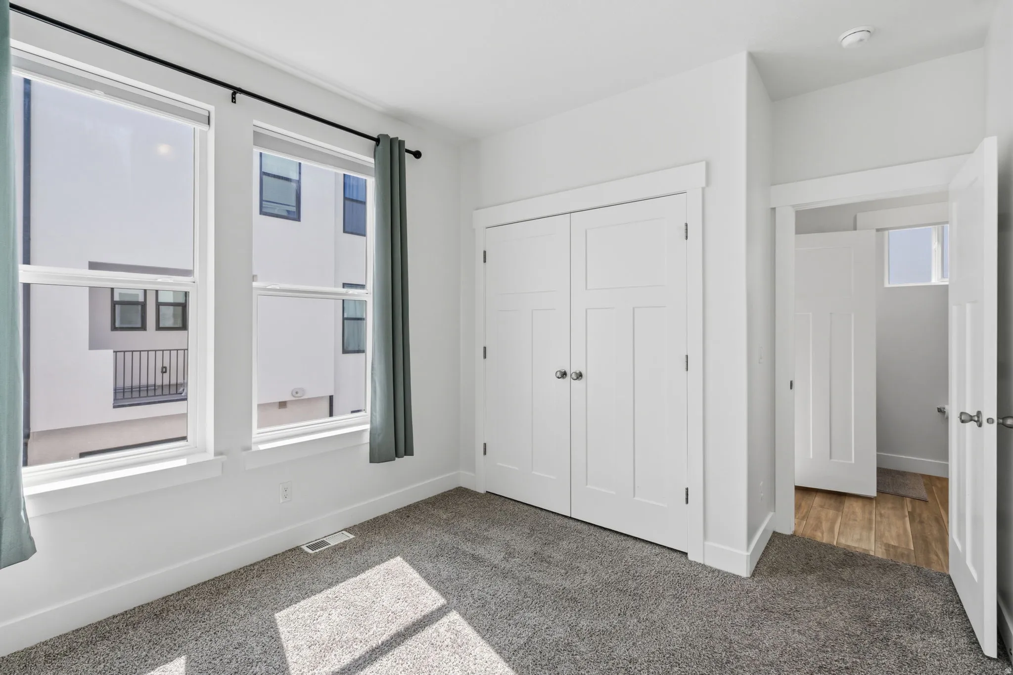 Spacious room featuring two large windows, plush grey carpeting, and white baseboards