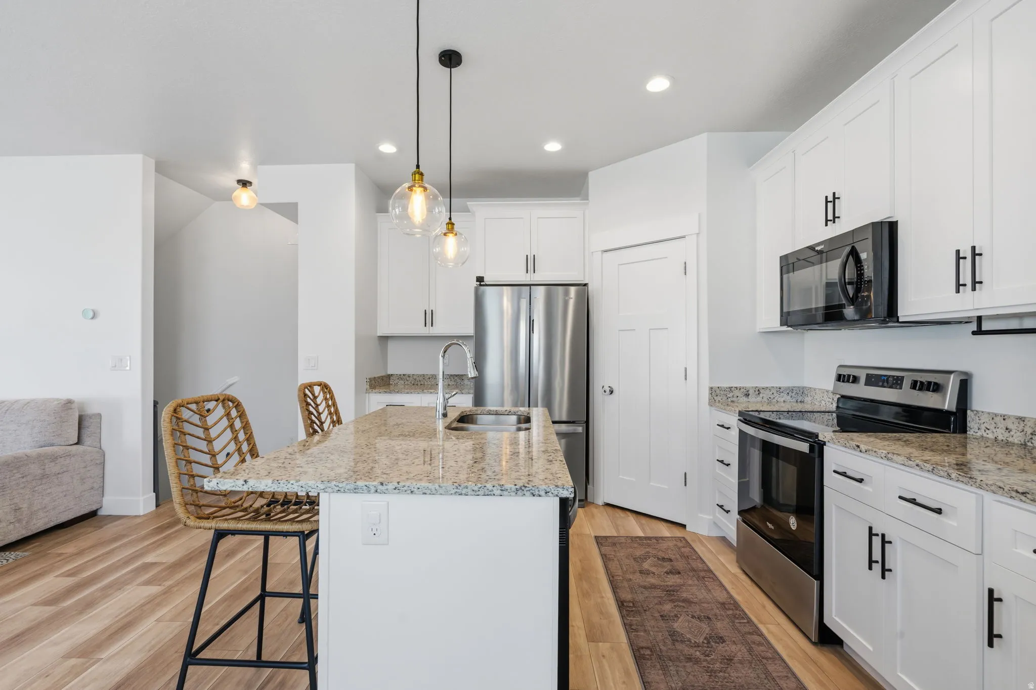 Kitchen featuring white shaker cabinetry, stainless steel appliances, granite countertops, and wood-finish flooring