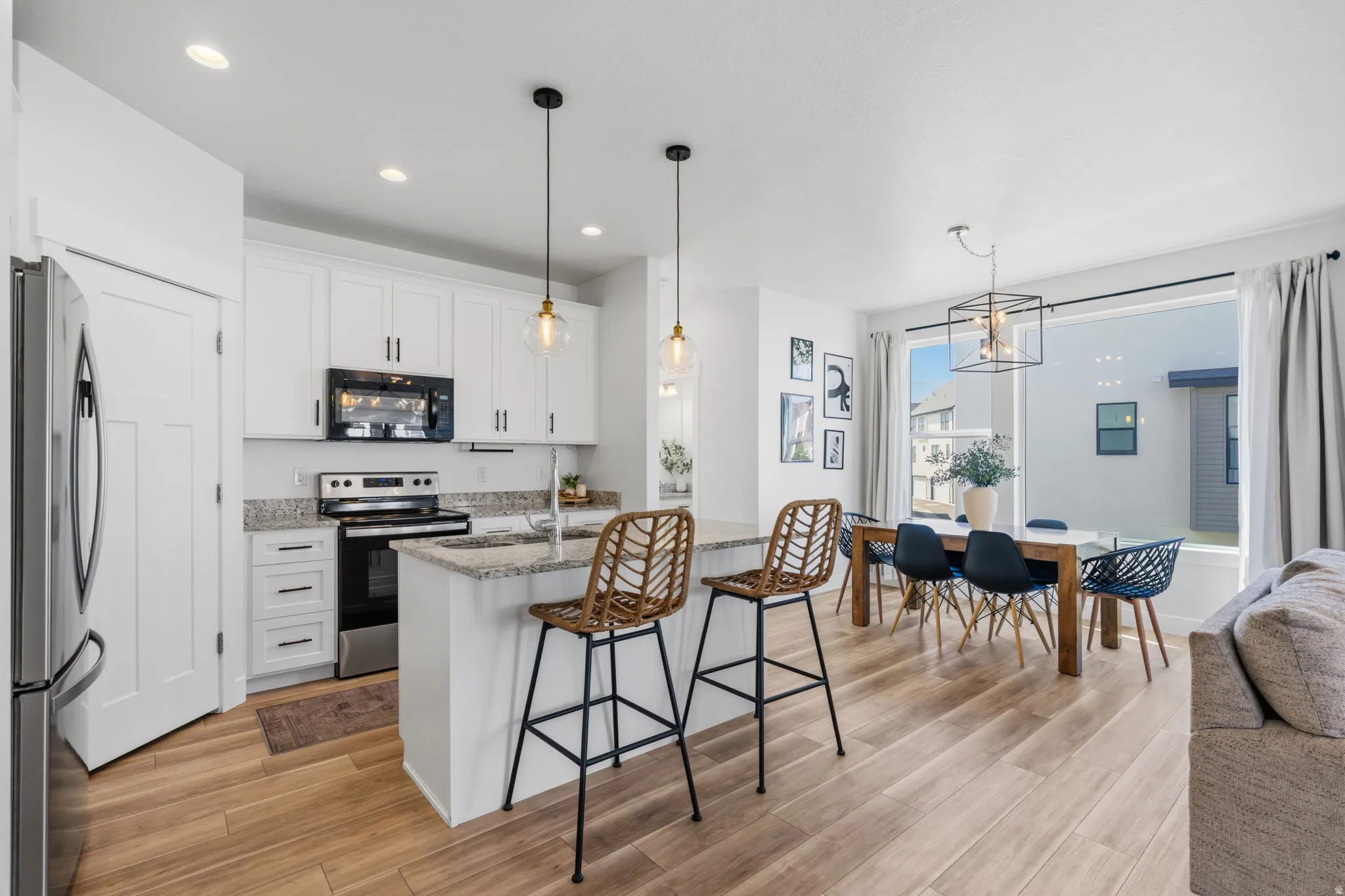 Open-concept living space featuring a kitchen island with pendant lighting, wood-finish flooring, white cabinetry, stainless steel appliances, and a dining area with a large window