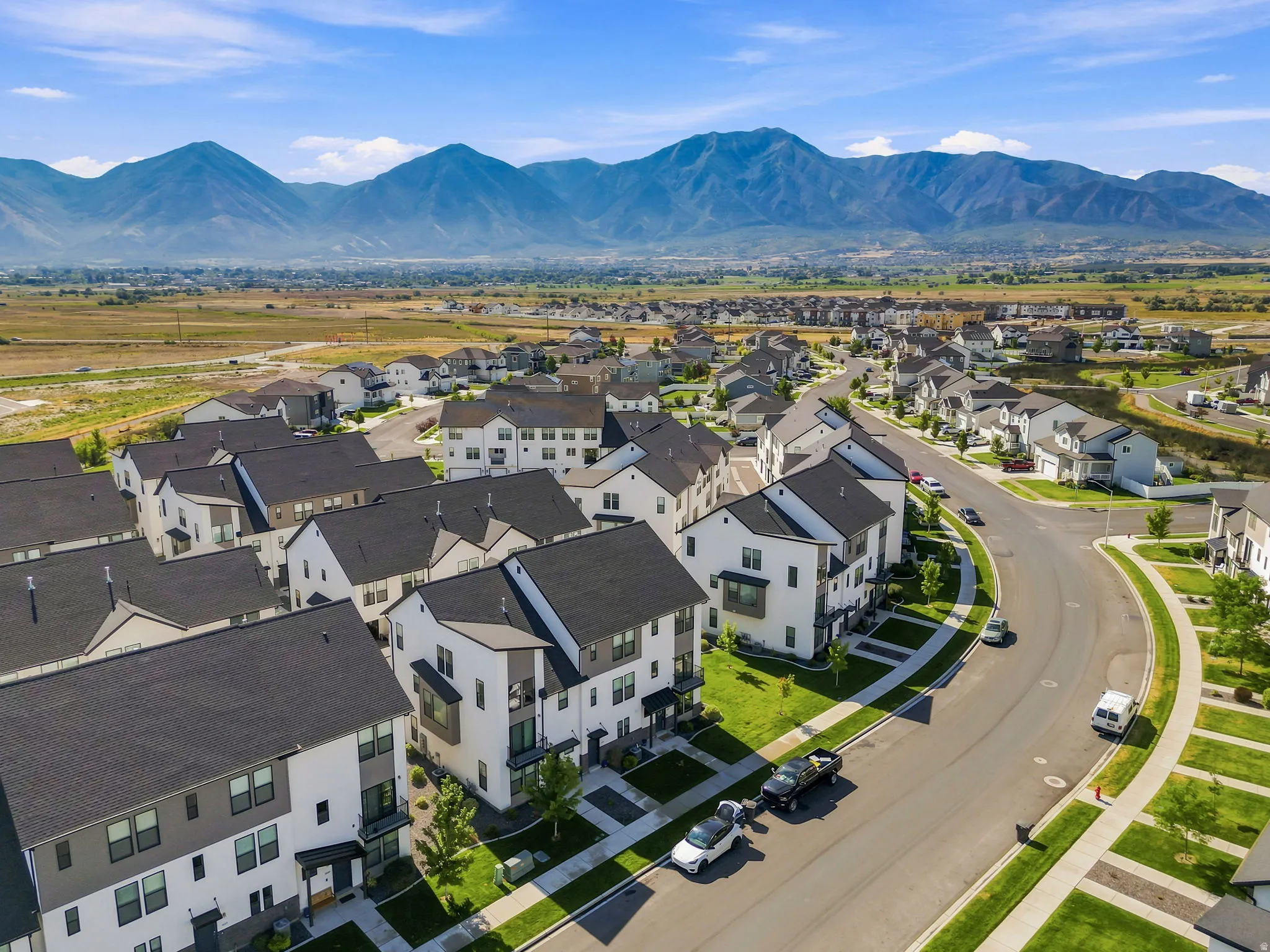 Modern residential neighborhood with mountain scenery, featuring contemporary architecture, paved streets, and manicured landscaping