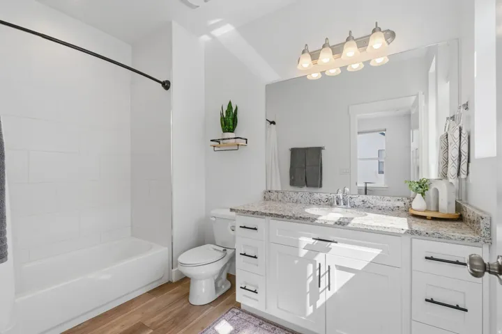 Bathroom featuring a white subway tile tub surround, wood-finish flooring, a white vanity with a light-colored countertop, and a large wall-mounted mirror