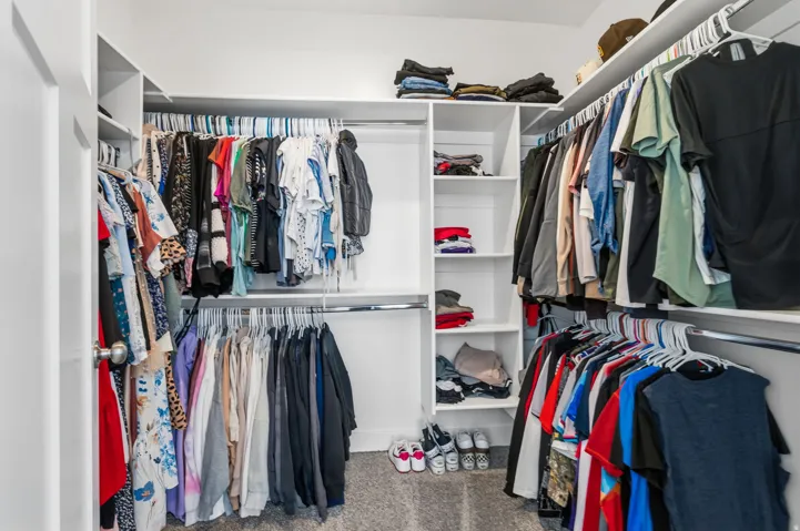 Walk-in closet featuring white built-in shelving, multiple hanging rods, and carpet flooring